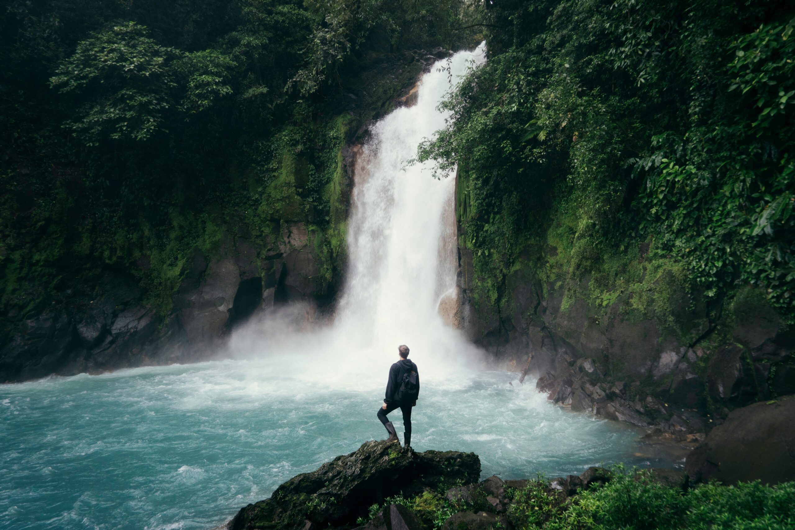 man standing on cliff near falls